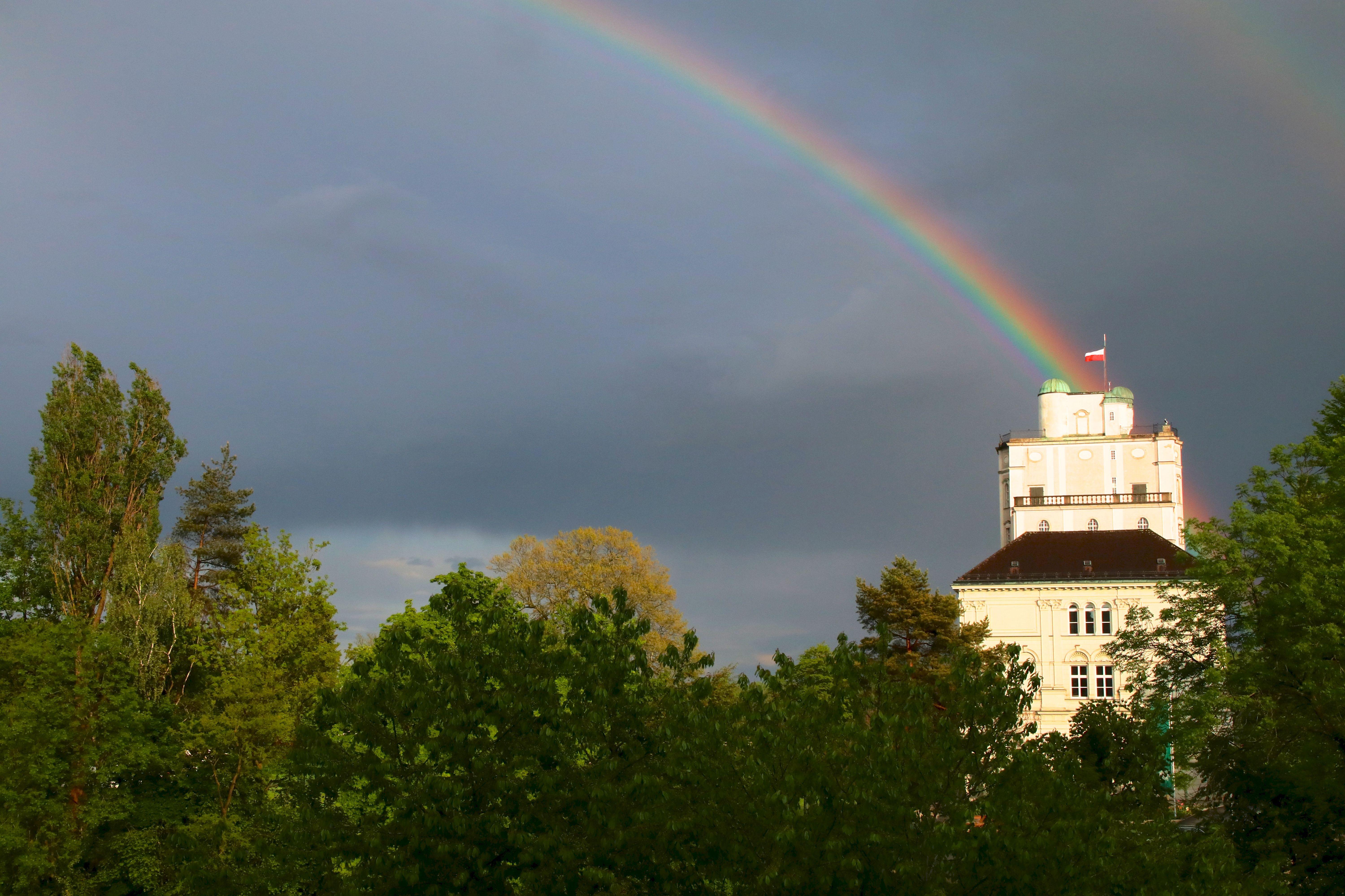 Ein intensiver Regenbogen leuchtet am dunklen Himmel über der Sternwarte und den Bäumen der Stiftsgärten