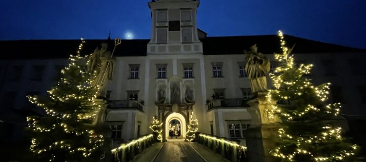 beleuchteter Torbogen mit Durchfahrt, rechts und links beleuchtete Christbäume