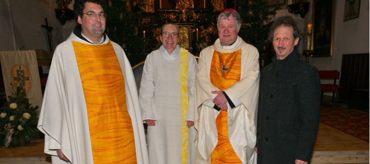 vier personen, davon zwei männer mit weiß-gelbem Priestergewand, eine Frau mit weißem Messgewand, ein Mann mit grauer Hose und schwarzer Jacke