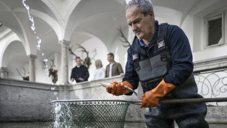 Ein Mann mit wasserfester Kleidung steht in einem Wasserbecken mit Kescher und einem Fisch in der Hand
