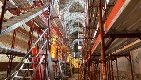 rotes Baugerüst im Inneren einer Kirche, nach oben hin Blick auf Stuck und Fresken