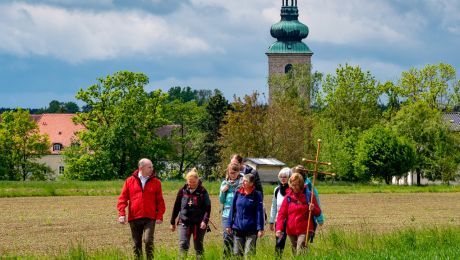 Kleine Pilgergruppe auf Wiesenweg mit Kirche im Hintergrund