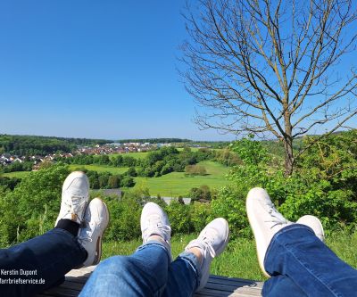 Die Beine dreier Jugendlicher sind hochgelegt: Jeans und weiße Sneaker zeigen Richtung satter Hügellandschaft